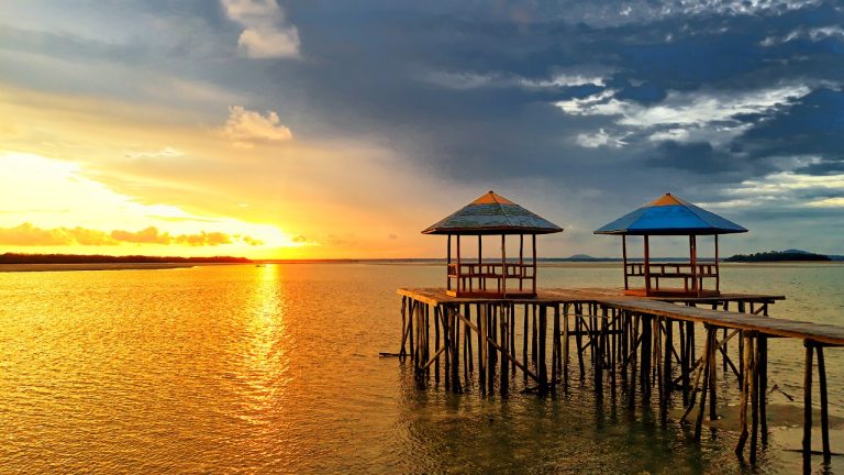 Sunset view over calm sea with wooden pier and gazebos at Gusong Bugis Mangrove Park, Belitung Island — tranquil golden-hour coastal landscape