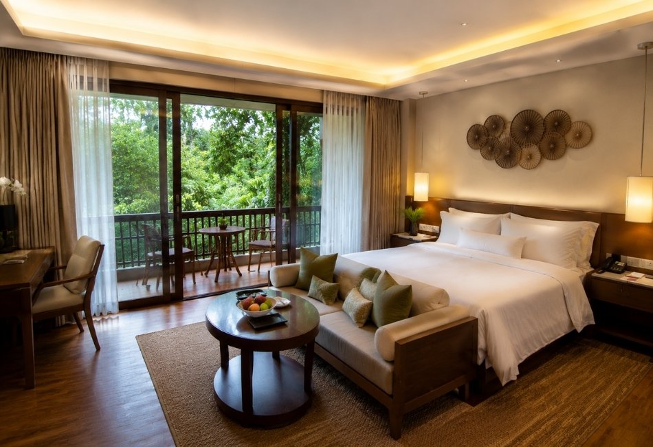 Warm modern resort bedroom with a cozy bed and greenery-facing balcony